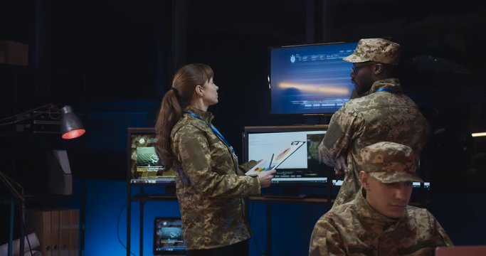 Caucasian woman militarian official coming to African American male general and bringing new information and data in documents about conflct in war zone. Man watching troops dislocation in office.