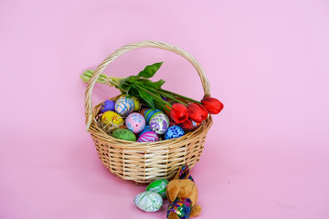 THe painted colorful Easter egg in the basket on the pink background copyspace to celebrate the traditional festival