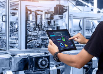Smart industry control concept.Hands holding tablet on blurred automation machine as background - obrazy, fototapety, plakaty