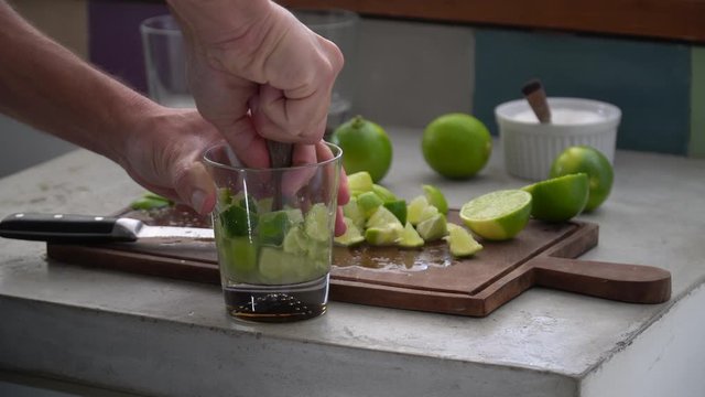 Close up of man hand preparing recipe for &ldquo;caipirinha&rdquo; drink with lime, sugar, ice and &ldquo;cachaca&rdquo; on kitchen countertop. The cacha&ccedil;a of Brazil is made of sugar cane. 4K