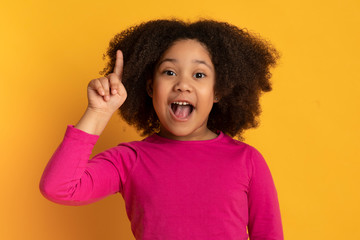 Idea concept. Little black girl pointing finger up over yellow background