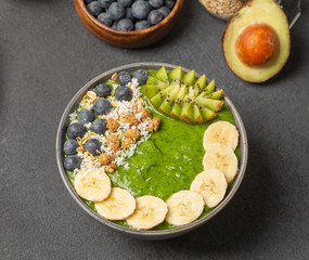 Healthy smoothie in the bowl from avocado and spinach with blueberries, mulberry, banana, granola, coconut and kiwi. Delicious breakfast.