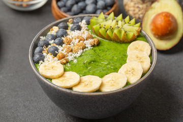 Healthy smoothie in the bowl from avocado and spinach with blueberries, mulberry, banana, granola, coconut and kiwi. Delicious breakfast.