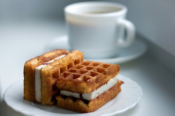 Two pieces of tasty Viennese waffles with cream on a plate with a cup of fresh coffee in the background by the window