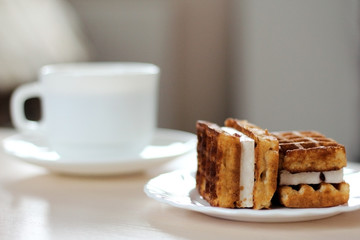 Two pieces of tasty Viennese waffles with cream on a plate with a cup of fresh coffee on a soft background on the table