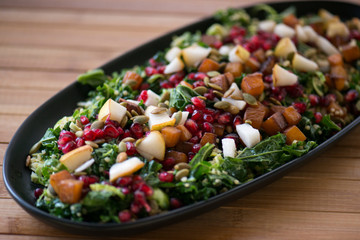 Winter salad with pomegranates, pears, kale sweet potato and pumpkin seeds served on a black serving plate in a beautiful setting