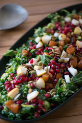 Winter salad with pomegranates, pears, kale sweet potato and pumpkin seeds served on a black serving plate in a beautiful setting