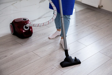 A girl in jeans and white socks is vacuuming the floor. Red vacuum cleaner.