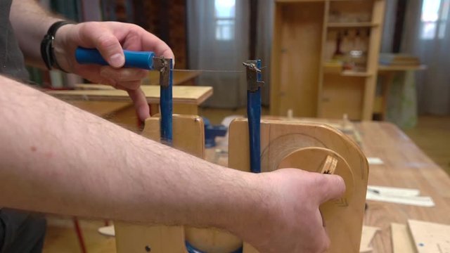 person hands fix fretsaw in wooden support on table demonstrating poor sawing tension before making jetliner model closeup