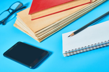 Heap of magazines, newspapers or some documents and red apple, notepad, pencil, glasses, smartphone on blue desk. Concept of education or back to school. Workplace of journalist or secretary