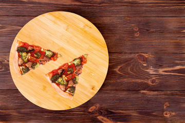 Two slices of pizza with veggie vegetables, on bamboo bottom, on wooden table, top view space for text