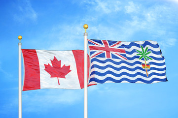 Canada and British Indian Territory two flags on flagpoles and blue cloudy sky