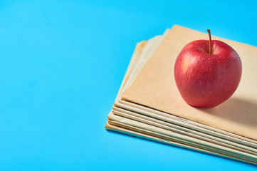 Heap of blank magazines, newspapers or some documents and red apple on blue desk. Concept of...