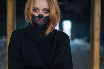 beauty portrait of a beautiful girl in a black mask with rhinestones, designer makeup. Emotionally posing. Against the background of the destroyed building. posing model. The concept of coronavirus