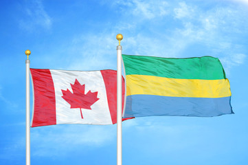 Canada and Gabon two flags on flagpoles and blue cloudy sky
