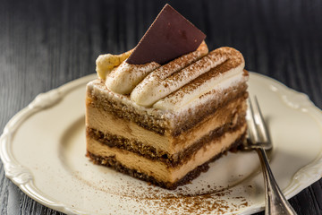 portion of chocolate and cream cake in white plate on wood