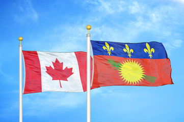 Canada and Guadeloupe two flags on flagpoles and blue cloudy sky