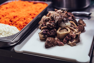 Boiled meat pieces with bones on white plastic cutting board, restaurant meal prepare