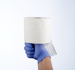 Right hand in blue glove holding with thumb a roll of toilet paper