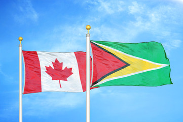 Canada and Guyana two flags on flagpoles and blue cloudy sky