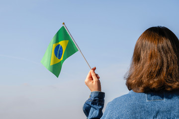 Woman hand with Brazil swaying flag on the blue sky. South America. Concept