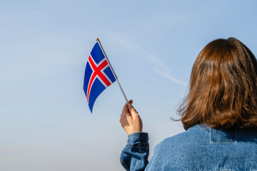 Woman hand with Iceland swaying flag on the blue sky. Concept