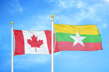 Canada and Myanmar two flags on flagpoles and blue cloudy sky