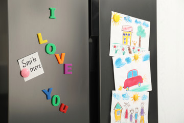 Modern refrigerator with child's drawings, note and magnets, closeup