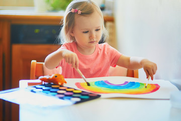 Girl drawing rainbow with colorful aquarelle paints