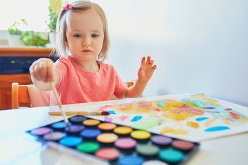 Girl drawing rainbow with colorful aquarelle paints