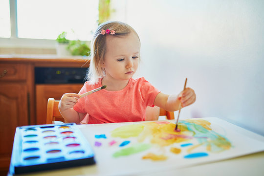 Girl drawing rainbow with colorful aquarelle paints
