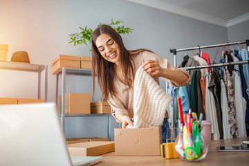 Young woman selling products online and packaging goods for shipping. Women, owener of small...