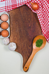 Wooden cutting board with red rug, spices, ladle, eggs and garlics