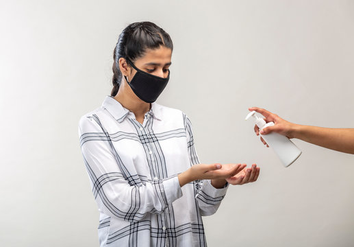 A teenage girl with protective mask on face using sanitizer to clean her hands