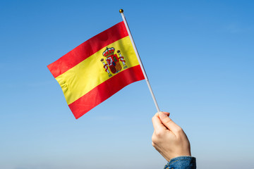 Woman hand with Spanish swaying flag on the blue sky. Spain. Concept