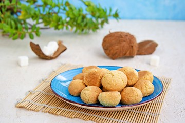 Ball-shaped sweet coconut cookies on a blue clay plate on a light concrete background. Coconut Baking