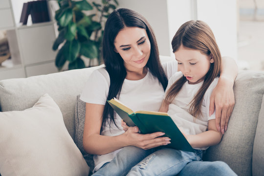 Portrait of two brown haired people lovely caring mother teach her daughter read book girl concentrated sit divan couch in living room house