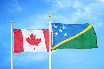 Canada and Solomon Islands two flags on flagpoles and blue cloudy sky