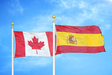 Canada and Spain two flags on flagpoles and blue cloudy sky