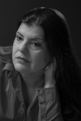 Lady closeup headshot portrait. She is in her 40s, has long smooth black hair. She is wearing a casual shirt. She has a hand behind her head as thinking. This is a black and white image.