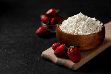 fresh homemade cottage cheese in a wooden plate with strawberries on a cutting board, healthy breakfast on a black table