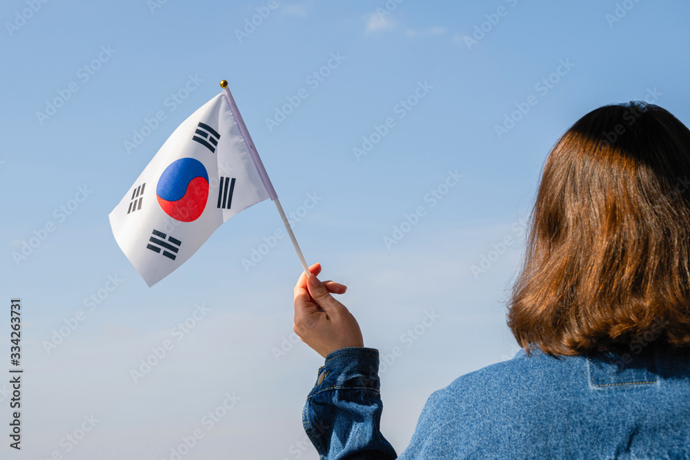 Wall mural Woman hand with South Korea swaying flag on the blue sky. Concept