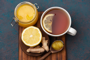 Hot tea, lemon, ginger roots and honey on dark wooden background. Alternative medicine still life.