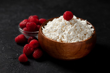 fresh homemade cottage cheese in a plate with raspberries on a dark background, healthy breakfast on a black table