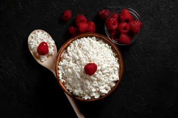 fresh homemade cottage cheese in a plate with raspberries on a dark background, healthy breakfast on a black table, top view