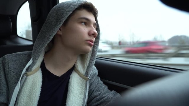A teenager rides in the back seat of a car and looks out the window, then is distracted by the phone to which the message arrived. The camera is shaking slightly