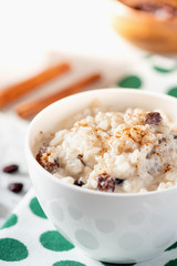 Rice pudding with raisins and cinnamon in a white ceramic bowl on a served table.