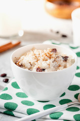 Rice pudding with raisins and cinnamon in a white ceramic bowl on a served table.