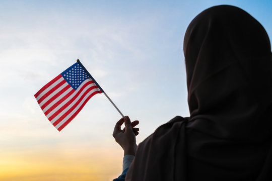 Silhouette of muslim woman in scarf with American, flag of at sunset. America. Concept