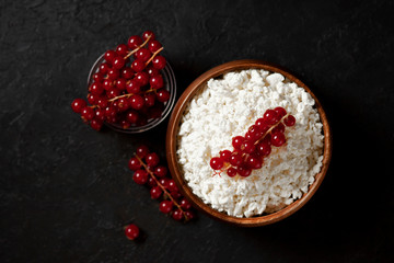 homemade cottage cheese with currants in a wooden plate against a dark background, a healthy milk breakfast with berries on a black table